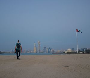 Full length rear view of man walking at beach by united arab emirates flag