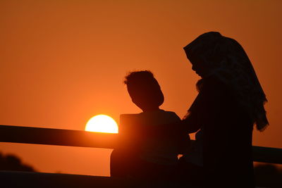 Silhouette mother and son standing against orange sky