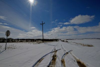 Snow covered road amidst field against sky during winter