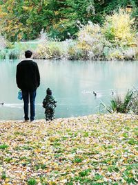 Rear view of man standing by lake against trees