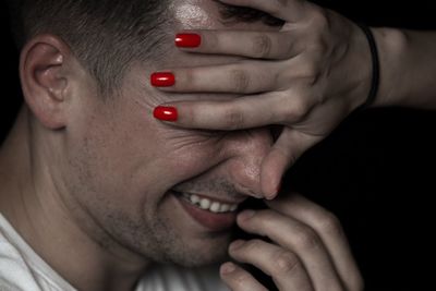 Cropped hand of woman covering happy boyfriend eyes against black background