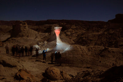 People on rock formation against clear sky at night