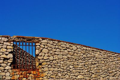 Low angle view of old stone wall against clear blue sky during sunny day