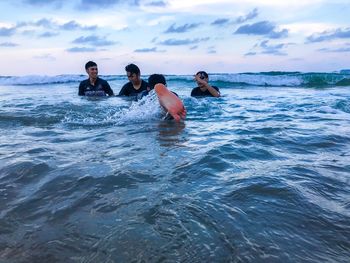 Friends swimming in sea against sky during sunset