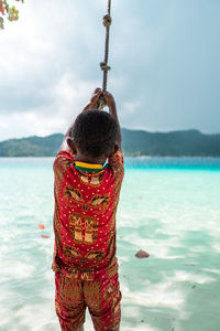 Rear view of man standing in sea against sky