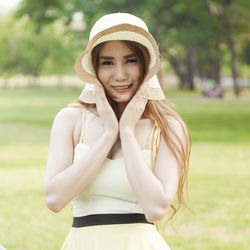 Close-up of young woman holding hat while standing on grass field