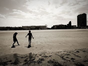 People walking on beach in city against sky