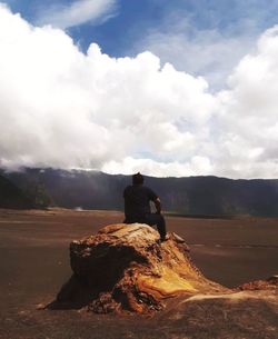 Man sitting on rock against sky