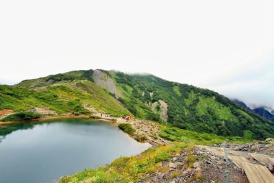 Scenic view of green mountain by lake against sky