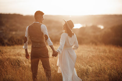 Rear view of couple standing on field during sunset