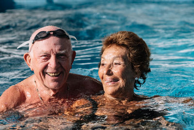 Cheerful senior couple smiling brightly while swimming together in outdoor pool during summer holidays