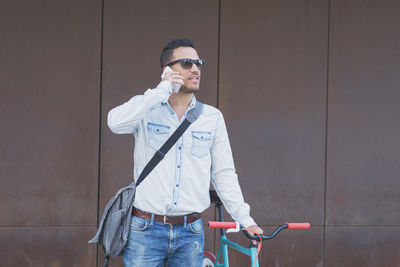Young man using phone while standing against wall