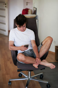 Teenage boy using phone while sitting on chair at home