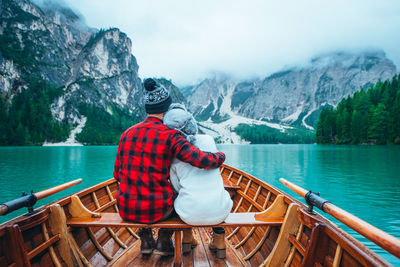 Rear view of man sitting on boat in lake against mountains