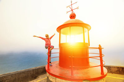 Woman with arms outstretched sitting on railing of lighthouse