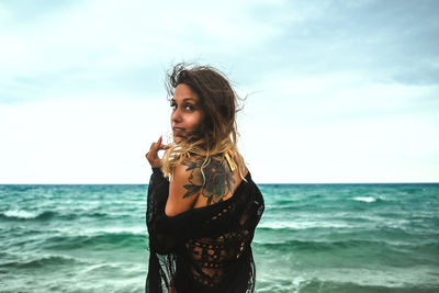 Young woman standing at beach against sky