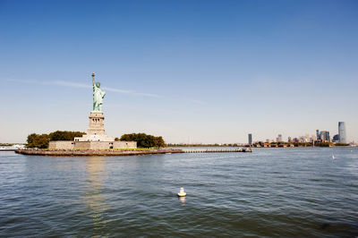 Statue of liberty on island against blue sky