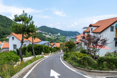 Road amidst trees and buildings against sky