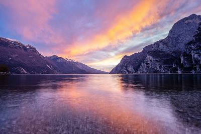 Scenic view of lake by snowcapped mountains against sky during sunset