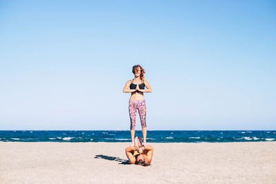Man and woman exercising on beach against sea and sky