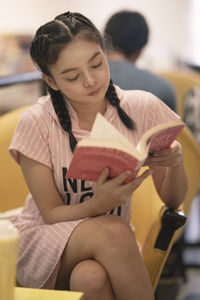 Teenage girl reading book while sitting at cafe