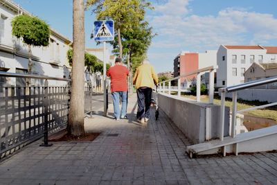 Rear view of people walking on footpath amidst buildings in city