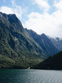 Scenic view of river and mountains against cloudy sky on sunny day