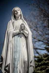 Low angle view of virgin mary statue against bare trees