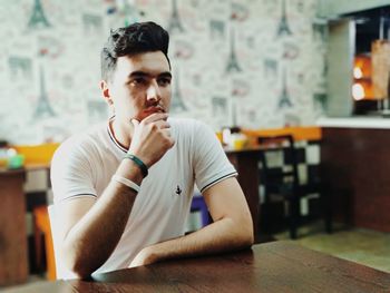 Thoughtful young man looking away while sitting at table in cafe