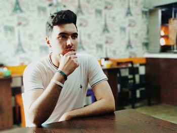 Portrait of young man looking away while sitting on table