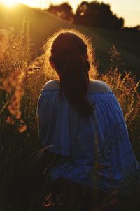 Rear view of woman standing on field against sky during sunset