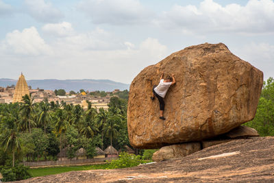 Man sitting on rock against sky