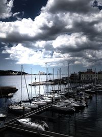 Boats in harbor against cloudy sky