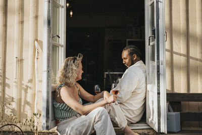 Man and woman enjoying wine while talking to each other sitting at cafe doorway