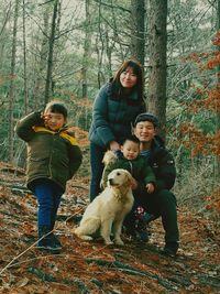 Smiling family with dog on field against trees in forest