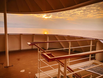 Empty chairs and table by sea against sky during sunset