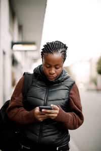 Teenage girl using smart phone while walking on footpath in city