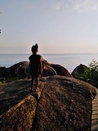 Man standing on rock looking at sea against sky