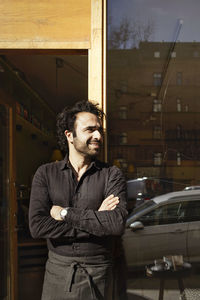 Smiling waiter looking away while standing outside coffee shop