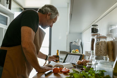 Mature man using digital tablet while standing at home in kitchen