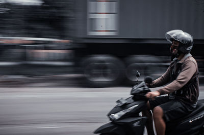 Blurred motion of man riding motorcycle on road in city