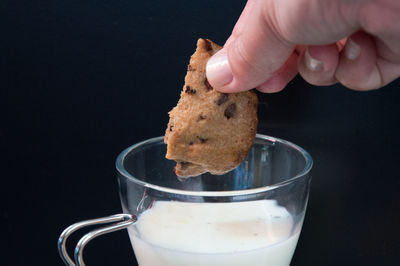 Close-up of hand holding chocolate cookie with black background