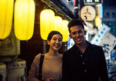 Portrait of smiling couple standing on street in city at night