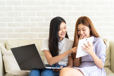 Young woman using phone while sitting on wall