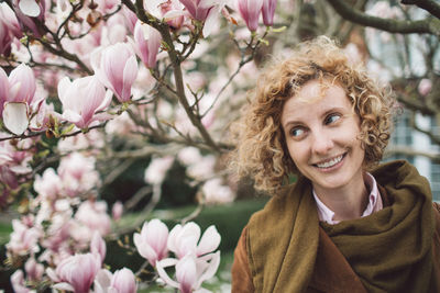 Smiling woman looking away against blooming flowers