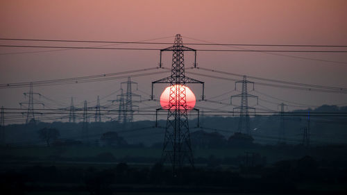 Low angle view of silhouette electricity pylon against sky during sunset