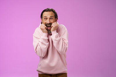 Portrait of young man standing against pink background