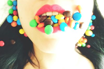 Midsection of woman with mouth covered with multi colored candies