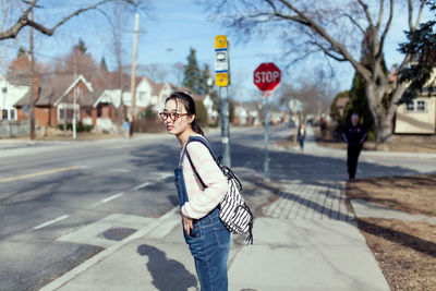 Side view of woman with backpack looking away while standing on sidewalk