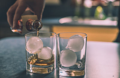 Close-up of hand pouring drink in glasses on table